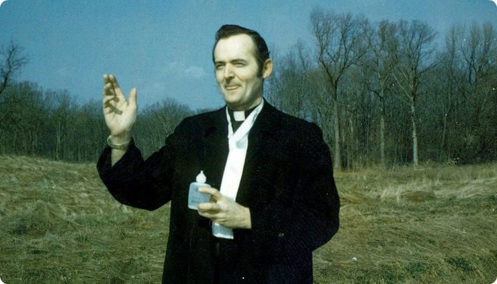 Father Hurley with Holy Water near a forest.
